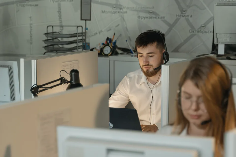 A man wearing a black headset in a professional office setting, working at a support desk.