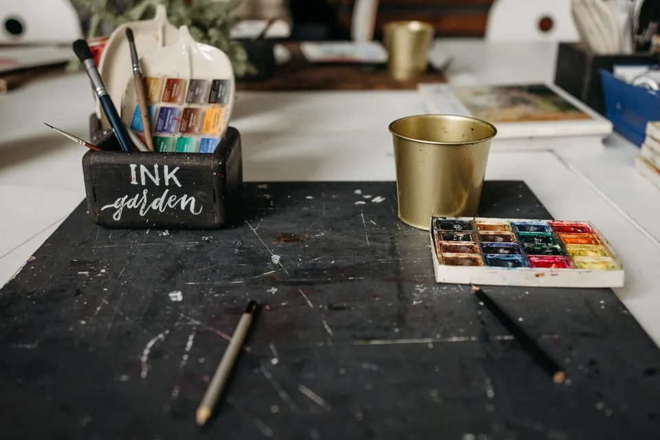 An array of paint pencils arranged in a bucket on a black board, evoking a creative workspace.