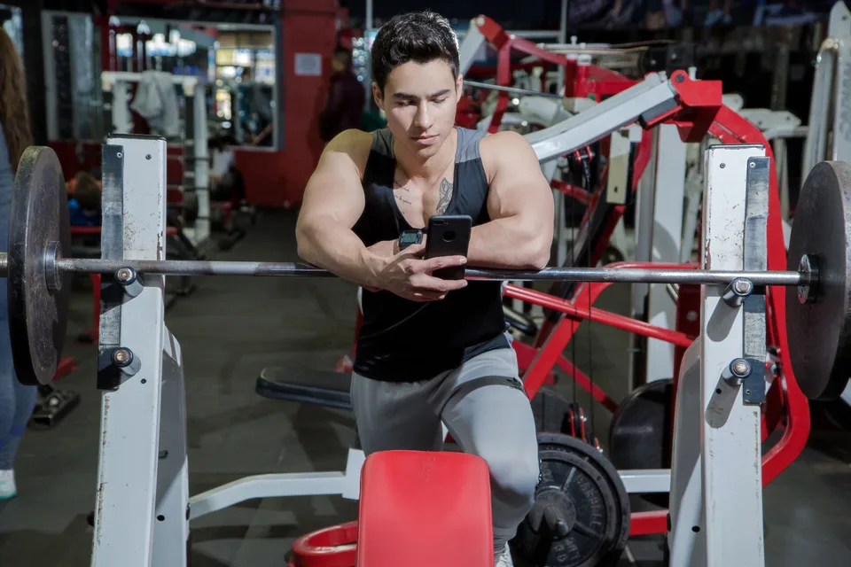 A man resting his hands on a barbell hung on a rack in a gym setting.