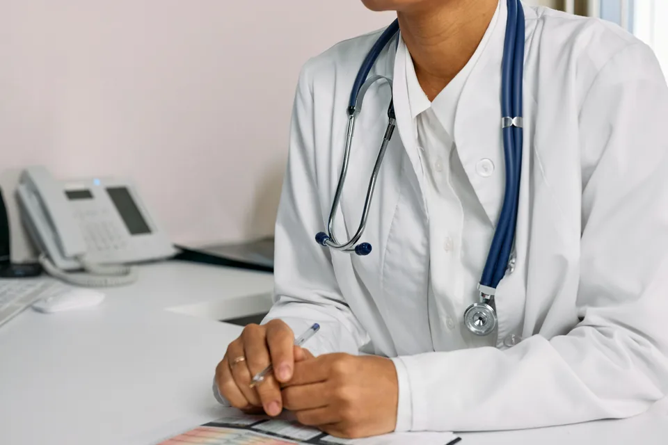A physician in a white coat working at a desk with a tablet and patient charts.