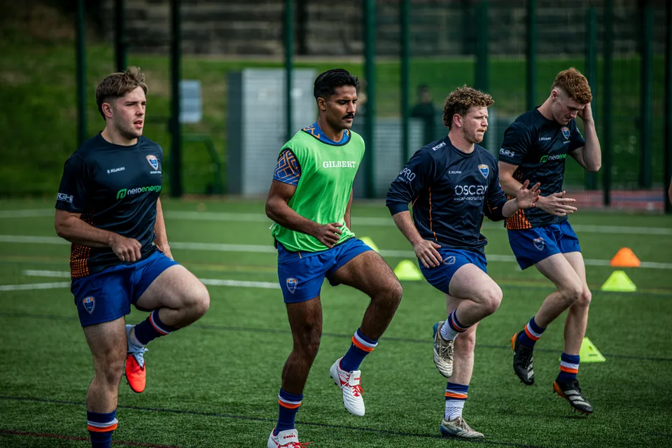 A rugby team training on a grass field with players running together.