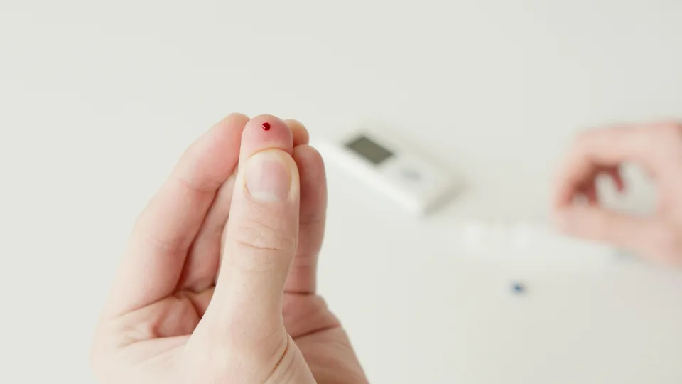 A finger with a small drop of blood from a glucose test.