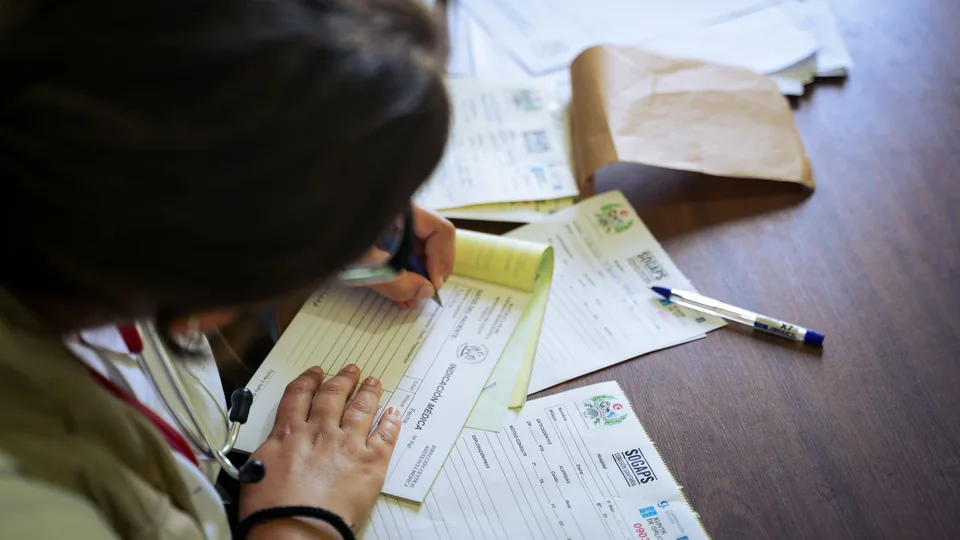 clinician filling out paper medical forms at a wooden desk