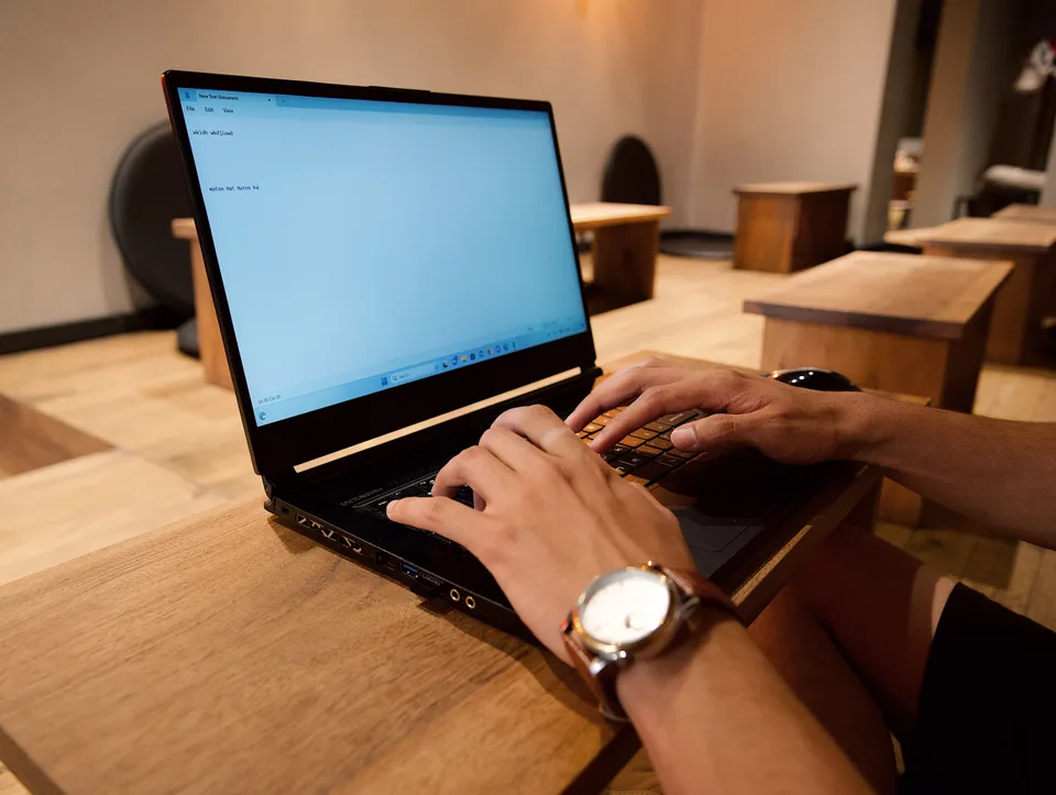 close-up of hands typing on a black laptop at a wooden table