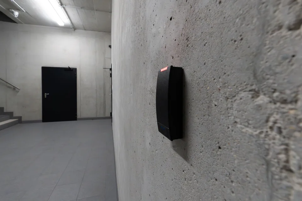 black keycard reader mounted on a concrete wall in an empty hallway leading to a closed door