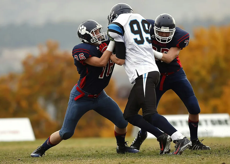 Two football players in pads and helmets running on the field during a game.