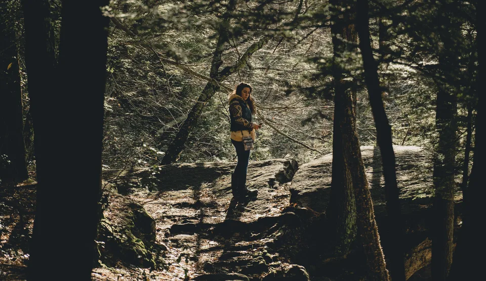 A woman standing peacefully near trees in a natural, wooded setting.