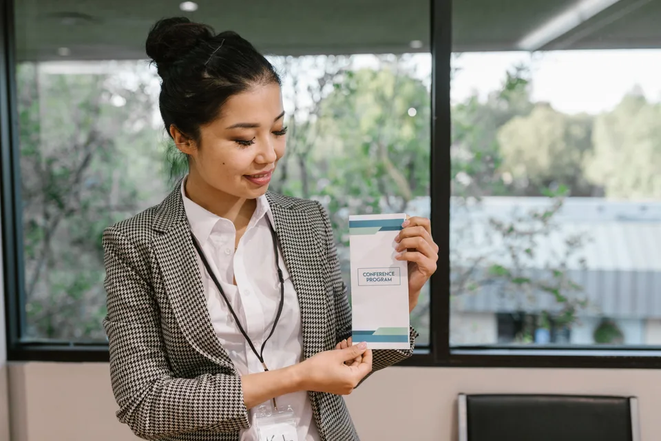 A woman in a black and white blazer holding an informational leaflet or brochure.