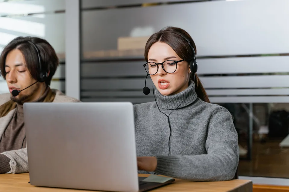 two customer support agents wearing headsets working at laptops in an office