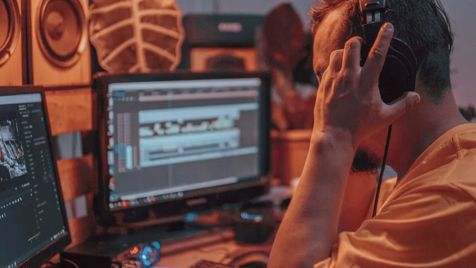 man wearing headphones editing audio and video on two computer monitors in a studio