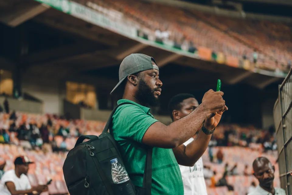 A man taking a photo on his phone at a sports event in a stadium.