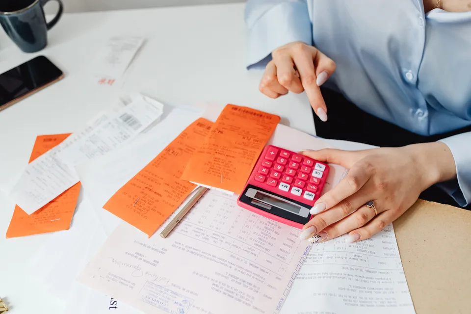 person holding a pink calculator over paperwork on a desk