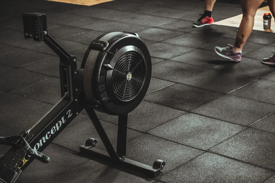 air rowing machine on a rubber gym floor with people walking past in the background