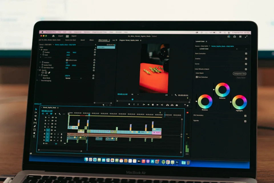 A person editing video footage on a laptop at a desk with a second monitor