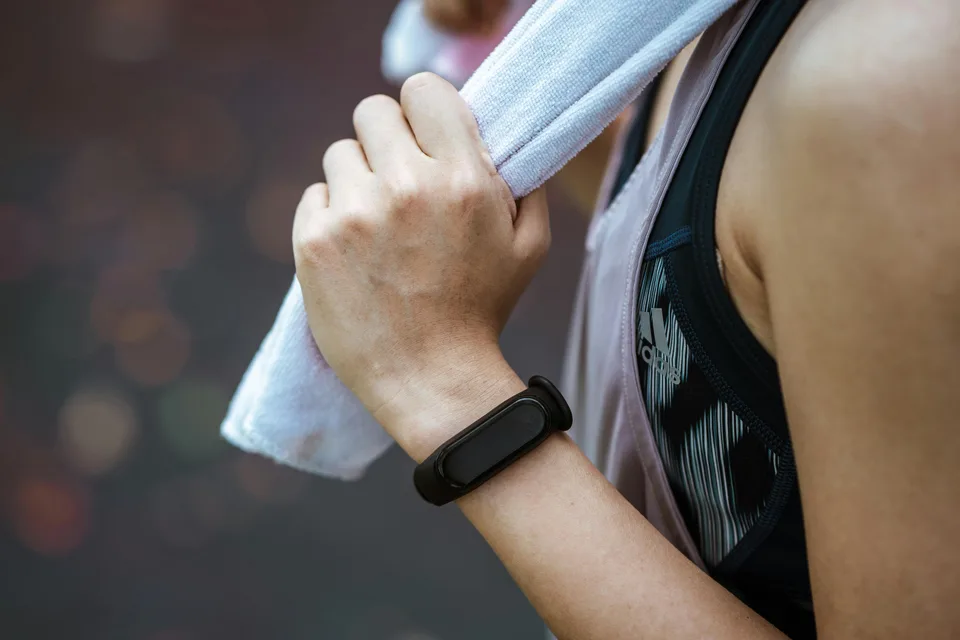 A woman wearing a smartwatch wiping her face with a towel after a workout.