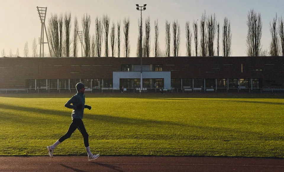 A runner training on a synthetic track at sunrise in an urban setting.