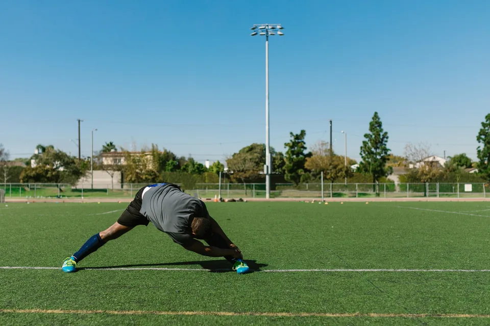 An athlete performing leg stretches as part of a warm-up routine in a training space.