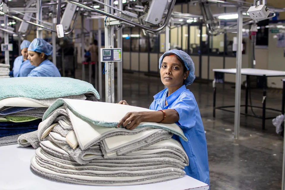 A female textile worker in an industrial factory setting, working alongside manufacturing equipment.