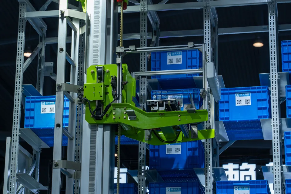 An automated warehouse robotic system moving blue storage crates along a conveyor path.