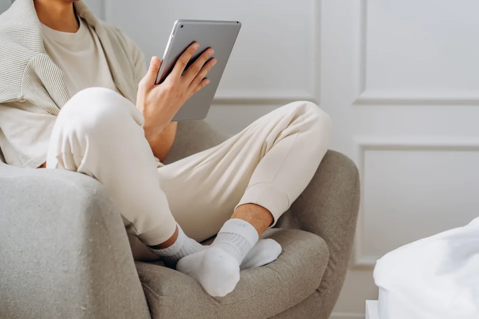 person sitting in a chair with legs crossed reading on a tablet