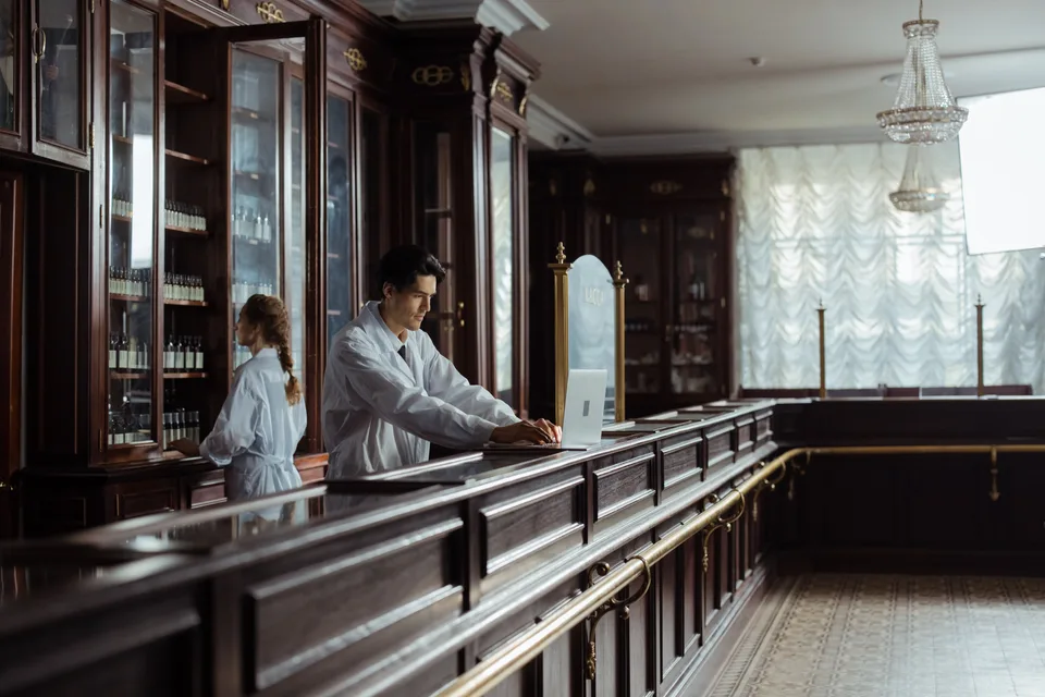 pharmacist working on a laptop at the counter of a traditional pharmacy