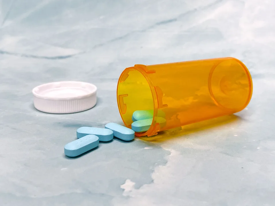 blue tablets spilling from an orange prescription bottle on a table