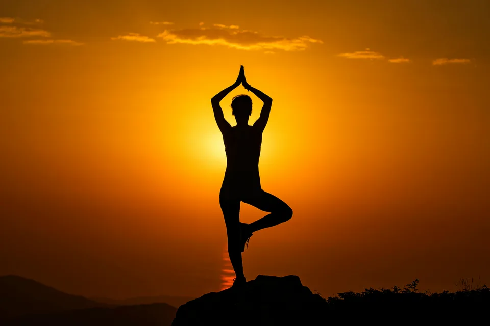 A silhouette of someone in a yoga pose at sunset against mountain landscape.