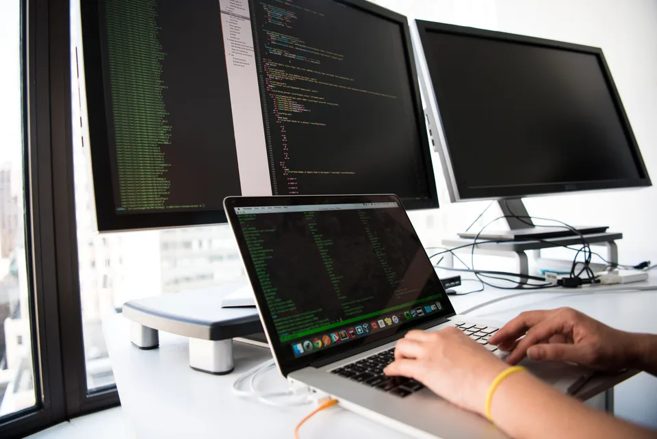A developer working at a desk with several monitors in a dimly lit office