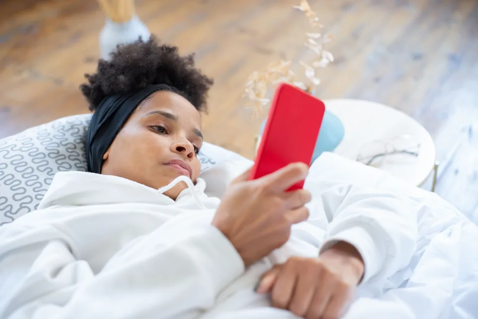A woman using a red cellphone, engaged with the device's screen.