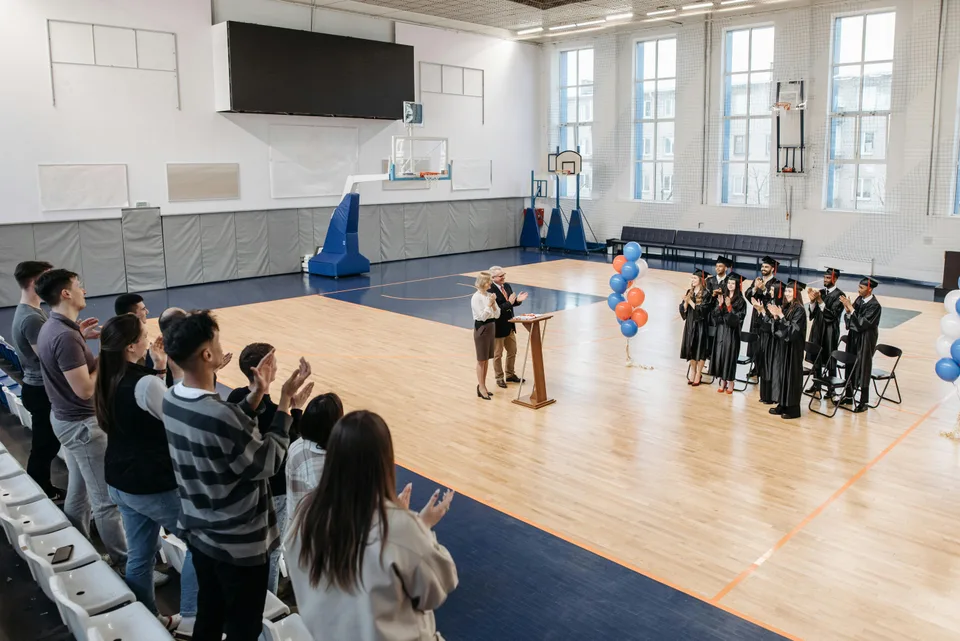 People gathered inside a college gymnasium watching a basketball game.