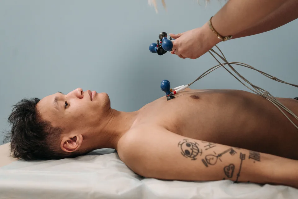 Patient lying on an exam table while a clinician attaches wired electrodes to his chest