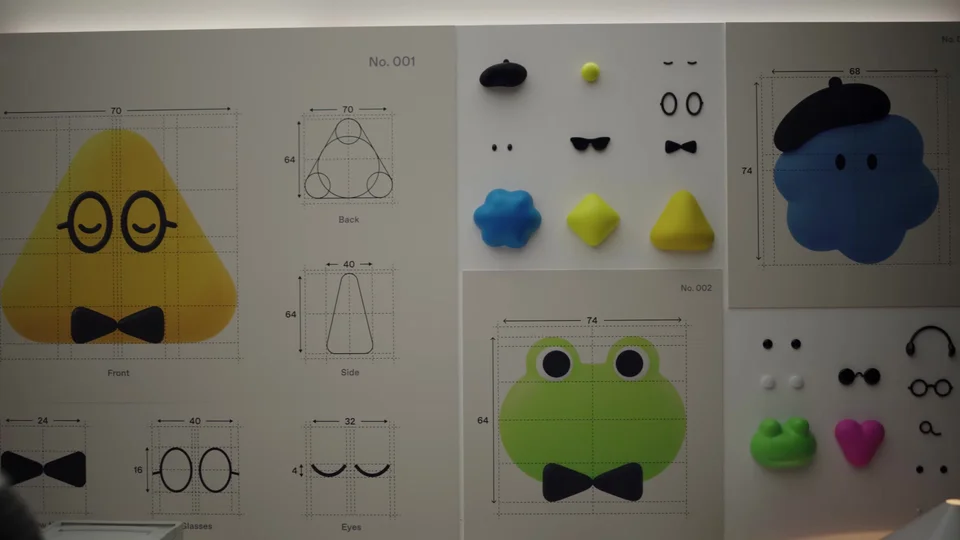 Design sheet of Dots characters: a yellow triangle with round glasses and a bow tie, a green frog with a bow tie, and a blue blob in a black beret, with interchangeable eyes, glasses and hats
