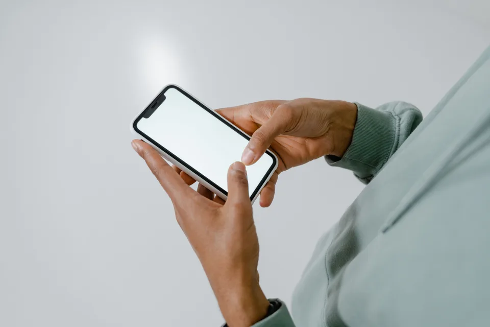 person holding a smartphone with a blank screen in front of a plain background