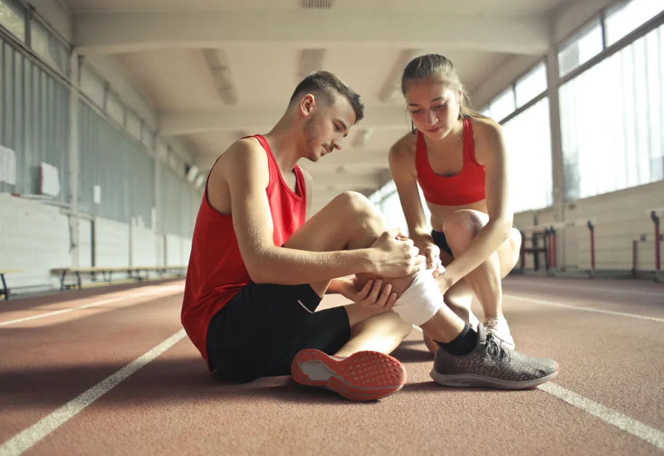 A woman wrapping a compression bandage around a man's leg in a recovery treatment setting.