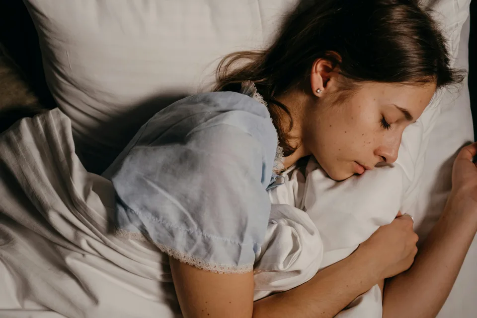 A person sleeping peacefully in soft early-morning light with a recovery-monitoring device nearby.