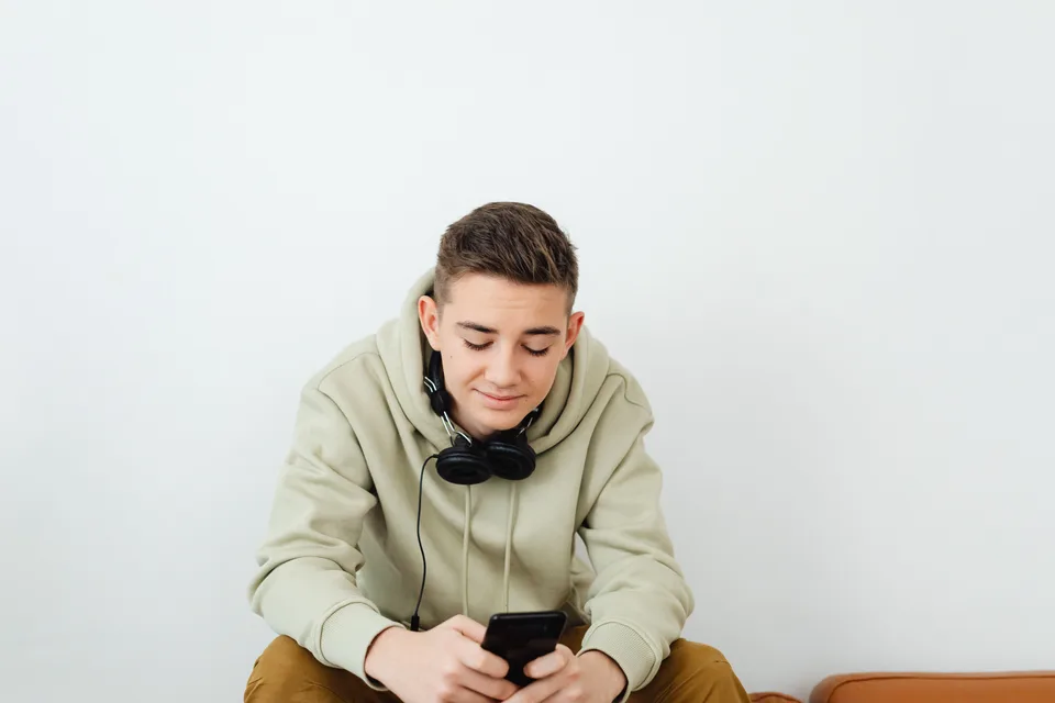 teenage boy in a hoodie with headphones around his neck looking down at a smartphone