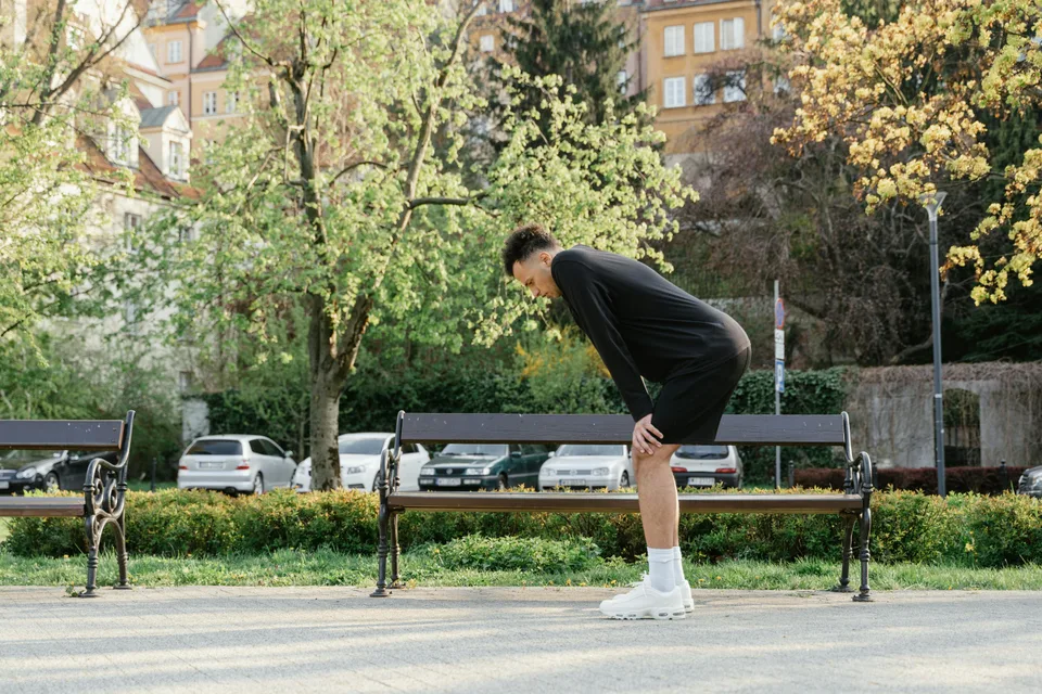 An athlete bent over resting their hands on their thighs, breathing heavily after exertion.