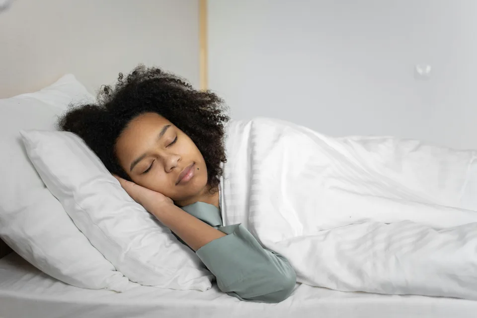A woman sleeping peacefully on a bed under a soft blanket.