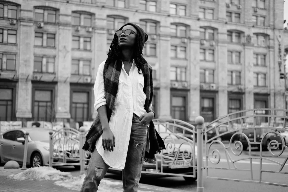 black and white photo of a woman in round sunglasses and a beanie standing on a city street