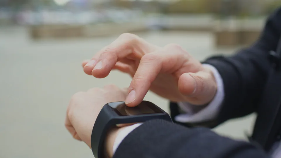 A person interacting with a modern smartwatch outdoors, wrist raised to check the display.