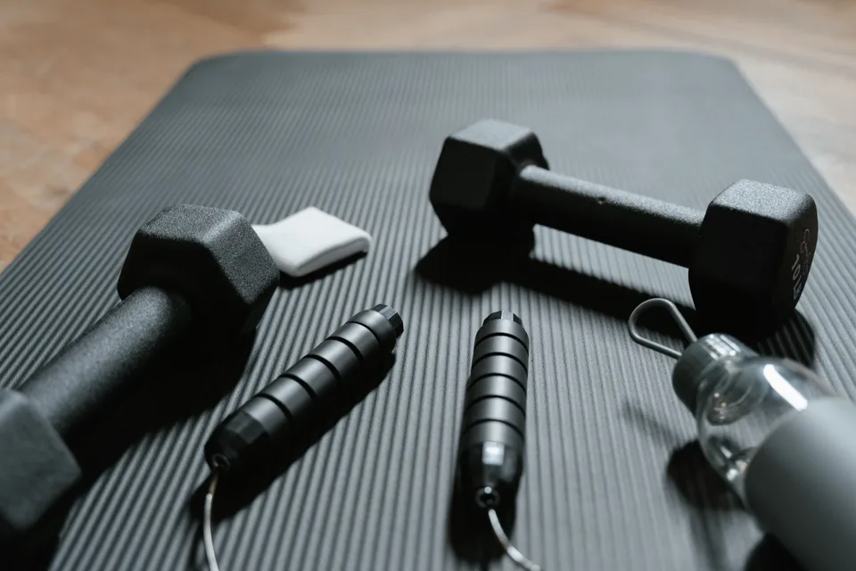 Dumbbells and a jump rope arranged on a yoga mat in a home workout setting.