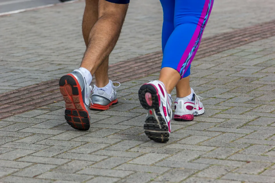 Two runners in sportswear running side by side on a sidewalk during a sunny day.