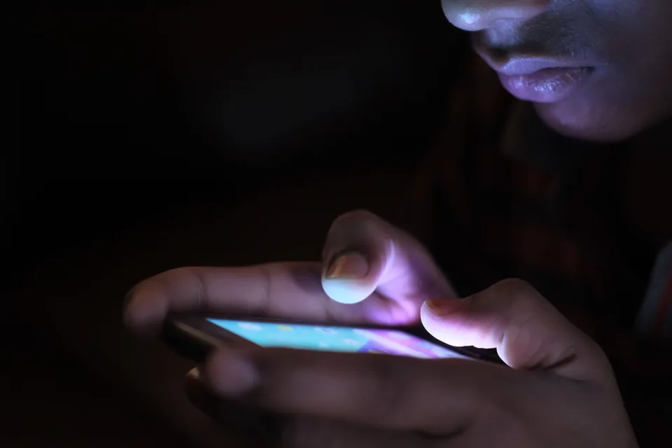 close-up of a person's hands holding a glowing smartphone in a dark room