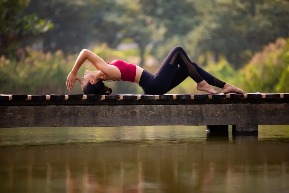 A woman practicing yoga on a jetty overlooking calm water, representing wellness and mindfulness.